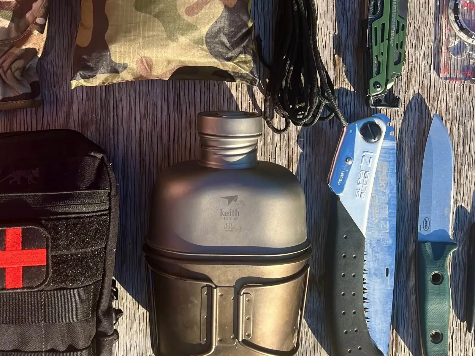 Contenuto di una bug out bag disposto a vista: borraccia, coltelli, multi-tool, kit di primo soccorso, bussola e paracord
